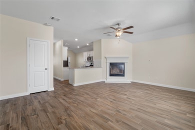 Unfurnished living room with a glass covered fireplace, dark wood-style floors, vaulted ceiling, a ceiling fan, and recessed lighting