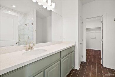 Full bath featuring a walk in closet, wood finish floors, a shower stall, vanity, and baseboards