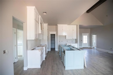 Kitchen featuring wood finished floors, white cabinetry, a kitchen island, and lofted ceiling