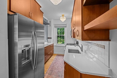 Kitchen featuring open shelves, stainless steel appliances, light wood-type flooring, brown cabinets, and light countertops