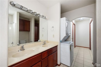 Full bath featuring tile patterned floors, toilet, stacked washer / drying machine, and a sink
