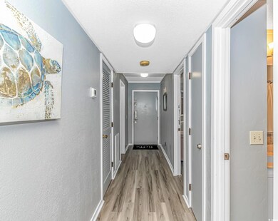Hallway with light wood-style floors, a textured wall, and a textured ceiling