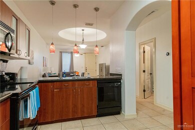 Kitchen with black appliances, dark countertops, light tile patterned floors, a sink, and arched walkways
