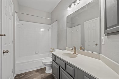 Full bathroom with a textured wall, shower / bathtub combination, vanity, and dark wood finished floors
