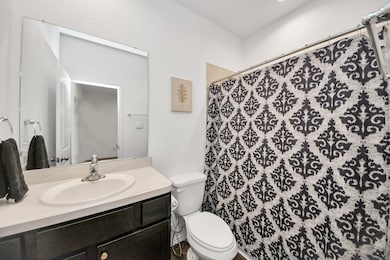 This contemporary bathroom offers a clean, stylish aesthetic with crisp white walls, dark cabinetry, and a sleek vanity with an integrated sink. A large mirror enhances the sense of space, while a patterned shower curtain adds a touch of personality. The modern finishes and thoughtful design make this bathroom both functional and visually appealing.