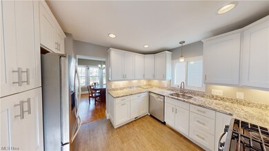 Kitchen featuring hanging light fixtures, sink, appliances with stainless steel finishes, light stone counters, and white cabinetry
