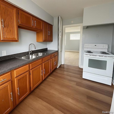 Kitchen featuring white range with electric cooktop, dark countertops, brown cabinets, and dark wood-style flooring