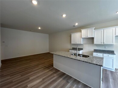 Kitchen with white cabinets, dark wood-style floors, light stone countertops, a kitchen island with sink, and recessed lighting