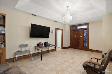 Entrance foyer with a tray ceiling, light tile patterned floors, and a chandelier