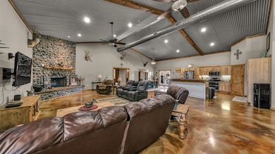 Living area featuring high vaulted ceiling, finished concrete floors, a stone fireplace, beamed ceiling, and ceiling fan