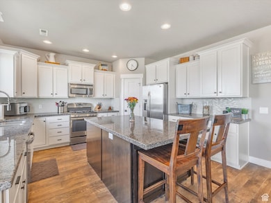 Kitchen featuring tasteful backsplash, white cabinets, appliances with stainless steel finishes, light stone countertops, and light wood-style floors