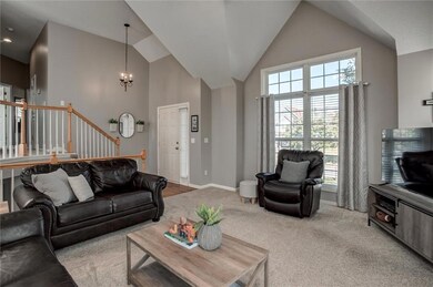Carpeted living room with high vaulted ceiling, a chandelier, and stairway