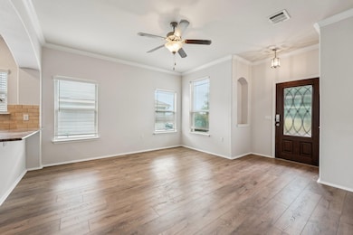 Entryway with hardwood / wood-style flooring, crown molding, a ceiling fan, arched walkways, and baseboards