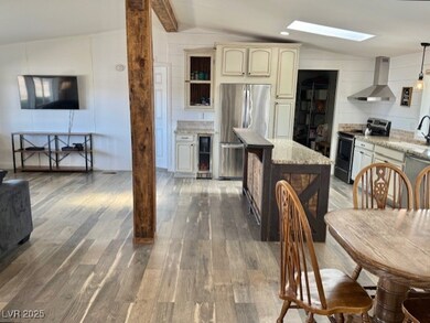 Kitchen with appliances with stainless steel finishes, lofted ceiling with skylight, wall chimney exhaust hood, and decorative light fixtures