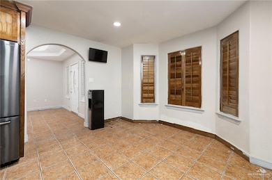 Empty room featuring recessed lighting, light tile patterned floors, baseboards, and arched walkways