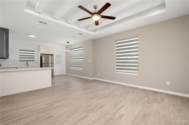 Unfurnished living room with sink, ceiling fan, a tray ceiling, and light wood-type flooring
