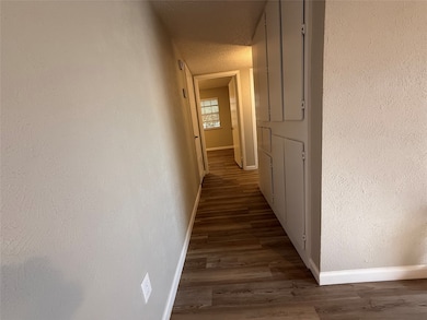 Hall with a textured wall, dark wood finished floors, and a textured ceiling