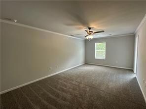 Empty room featuring crown molding, dark carpet, and ceiling fan