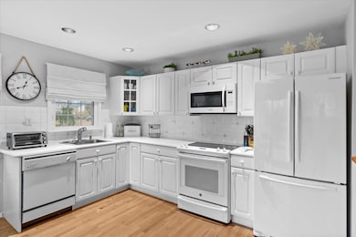 Kitchen featuring a sink, a toaster, light wood-style floors, white appliances, and light countertops