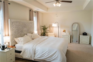Bedroom with carpet flooring, a tray ceiling, and ceiling fan