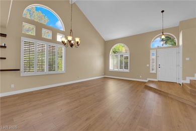 Foyer entrance featuring high vaulted ceiling, a chandelier, light wood-style flooring, and stairway