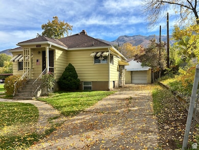 View of front facade featuring a mountain view, a chimney, an outdoor structure, a detached garage, and a shingled roof
