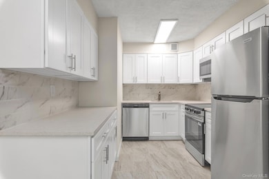Kitchen with stainless steel appliances, white cabinetry, a textured ceiling, tasteful backsplash, and light stone counters