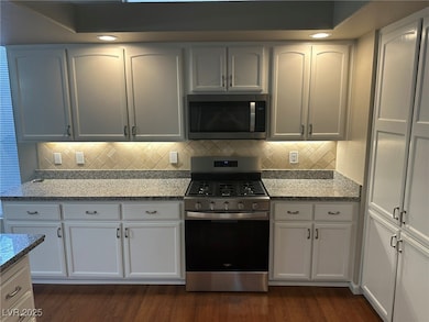 Kitchen featuring appliances with stainless steel finishes, light stone counters, and dark wood-type flooring