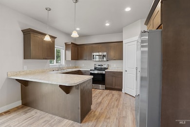 Kitchen featuring appliances with stainless steel finishes, light countertops, a peninsula, decorative light fixtures, and a breakfast bar