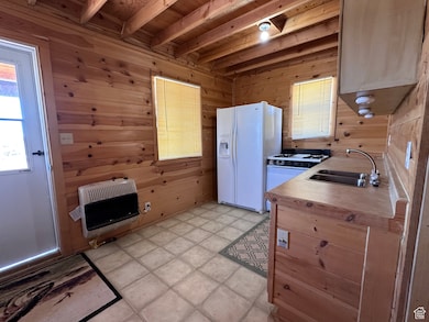 Kitchen featuring white appliances, heating unit, wooden walls, and sink
