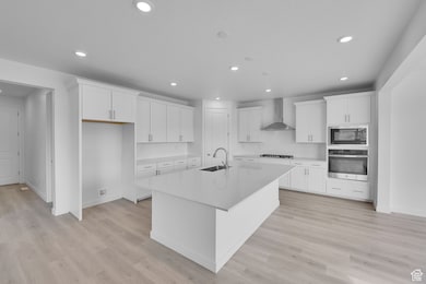 Kitchen with appliances with stainless steel finishes, white cabinetry, light wood-style flooring, an island with sink, and recessed lighting