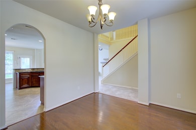 This room features hardwood flooring, large windows with blinds allowing natural light, neutral wall colors, and a modern overhead light fixture, creating a bright and welcoming space.