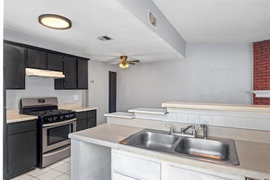 Kitchen with gas range, light countertops, light tile patterned floors, dark cabinets, and ceiling fan
