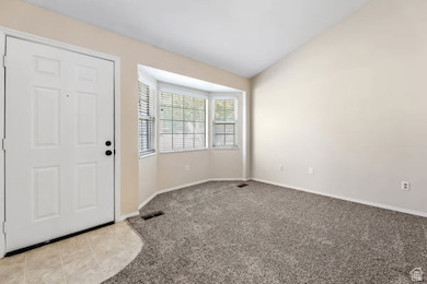 Entrance foyer with vaulted ceiling, light colored carpet, and light tile patterned floors