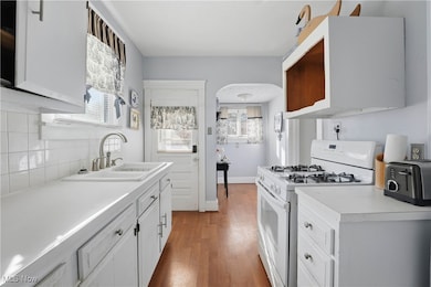 Kitchen featuring white gas range oven, light countertops, white cabinets, light wood finished floors, and arched walkways