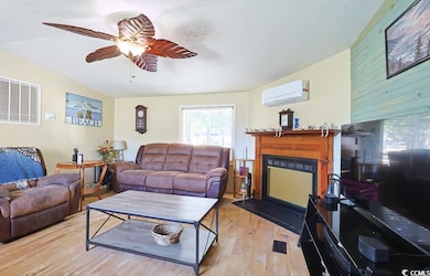 Living room featuring wood finished floors, a glass covered fireplace, an AC wall unit, a textured ceiling, and a ceiling fan