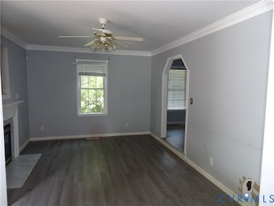 Unfurnished living room featuring crown molding, dark wood-type flooring, arched walkways, a ceiling fan, and a fireplace