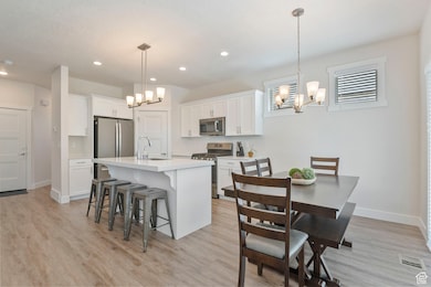 Kitchen with stainless steel appliances, a chandelier, a kitchen breakfast bar, light countertops, and light wood-style flooring