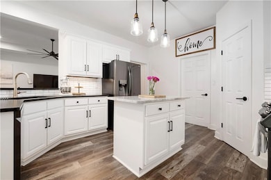 Kitchen featuring dark wood-type flooring, tasteful backsplash, a ceiling fan, hanging light fixtures, and white cabinetry