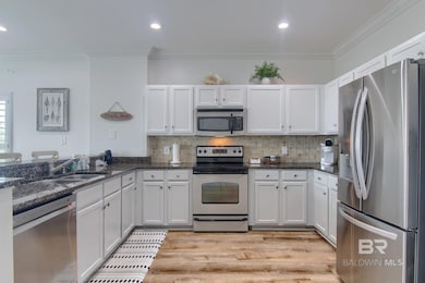 Kitchen featuring appliances with stainless steel finishes, ornamental molding, decorative backsplash, light wood finished floors, and dark stone counters
