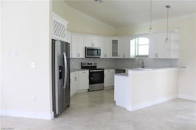 Kitchen featuring stainless steel appliances, a peninsula, tasteful backsplash, light stone counters, and white cabinetry