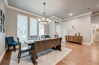 Dining area with light hardwood / wood-style flooring, crown molding, and an inviting chandelier