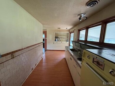Kitchen featuring a textured ceiling, wainscoting, washer / dryer, pendant lighting, and light wood-style floors