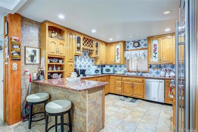 Kitchen featuring a kitchen breakfast bar, appliances with stainless steel finishes, light stone counters, glass insert cabinets, and a peninsula