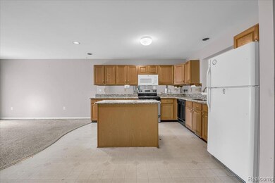 Kitchen featuring white appliances, brown cabinetry, light carpet, a kitchen island, and recessed lighting