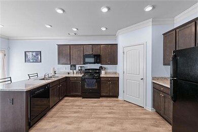 Kitchen with a peninsula, crown molding, dark brown cabinets, black appliances, and a sink