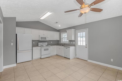 Kitchen featuring white appliances, a sink, lofted ceiling, white cabinets, and a textured ceiling