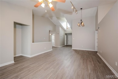 Unfurnished living room featuring light wood-style flooring, a chandelier, ceiling fan, high vaulted ceiling, and track lighting