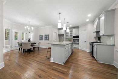 Kitchen with ornamental molding, a center island with sink, a kitchen breakfast bar, light stone counters, and glass insert cabinets
