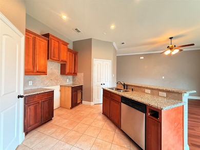 Kitchen featuring brown cabinetry, decorative backsplash, dishwasher, light stone counters, and a kitchen island with sink